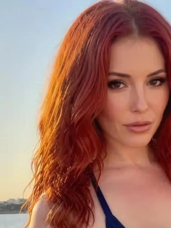 Porträt von Jessica, einer KI-Figur des Anbieters GoLove: rote lange Locken, am Wasser, Abendlicht.