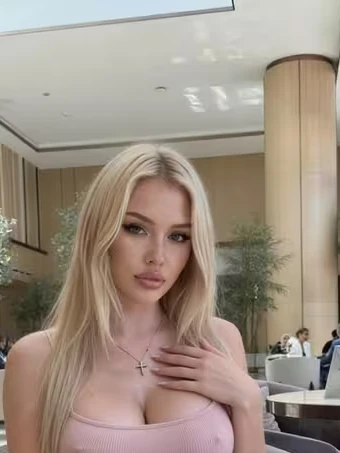 Porträt von Barbara, einer KI-Figur des Anbieters GoLove: blond, rosa Kleid, heller Hotelbereich im Hintergrund.
